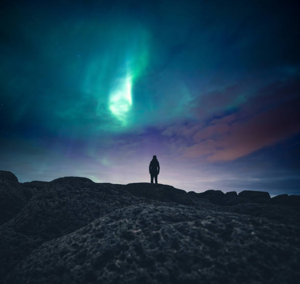 Under The Northern Lights Woman standing on the coast and watching aurora borealis. geomagnetic storm photos stock pictures, royalty-free photos & images