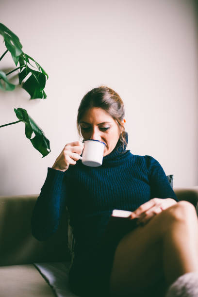 istock Beautiful young woman reading a book and drinks coffee (toned image, selective focus) 954296630
