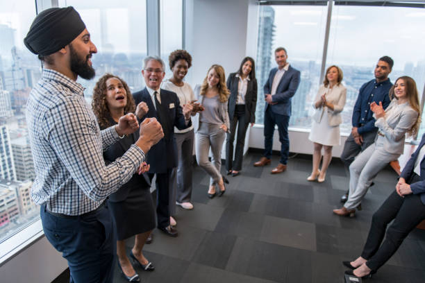 Team building in a high-rise city office A group of professionals stands in a semi-circle, laughing and clapping. turban stock pictures, royalty-free photos & images