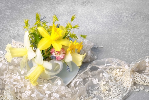 yellow narcissus and wild spring flowers bouquet in a coffee cup instead of vase with lace and copy space for your greetings text