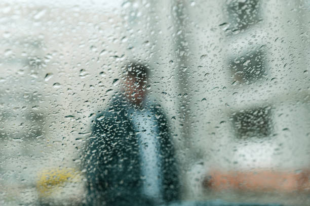istock wet rain drops on glass. man silhouette through wet glass 954334616