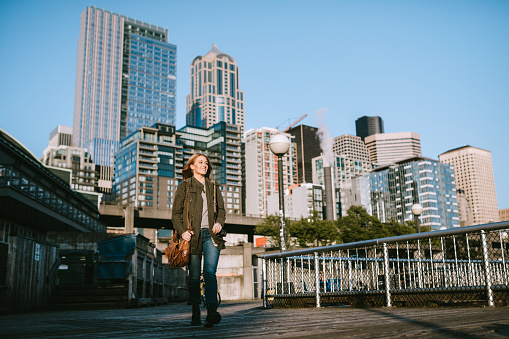 A woman walks on one of the piers of downtown Seattle, the cityscape visible behind her.