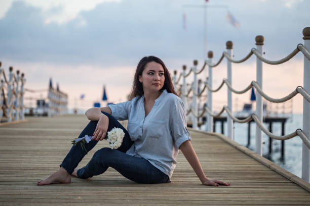 istock Female sitting by seaside at pier 954340840