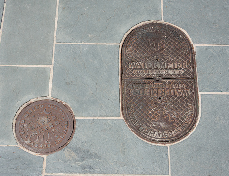 Ornate, old-fashioned, metal water meter covers on a sidewalk in the historic old town section of Charleston, South Carolina.