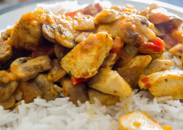 A close up of a chicken curry containing onions and peppers sitting on a bed of rice