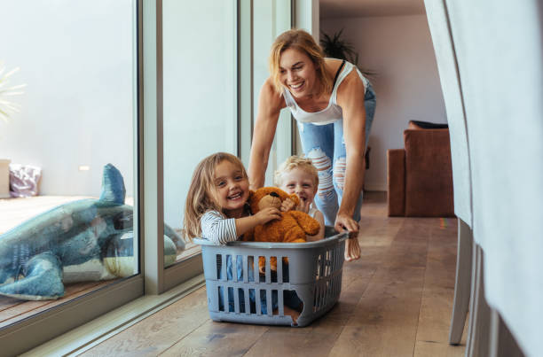 Mother playing with her children at home Happy young mother pushing children sitting in laundry basket. Mother and children playing at home. happy sibling day stock pictures, royalty-free photos & images