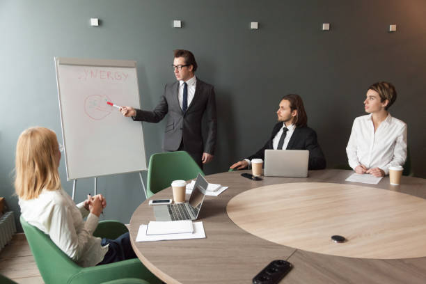 istock Confident speaker business coach gives presentation to team with flipchart 954357310