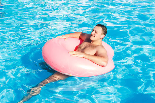 Young man is floating on inflatable air ring/circle in pool with blue water.