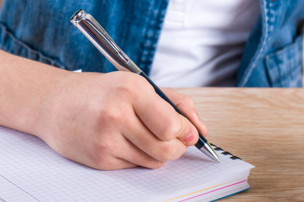istock Child's hand holding pen. The child writing letters in a notebook 954380242