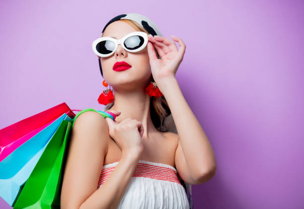 Portrait of beautiful style woman in sunglasses with shopping bags on purple background