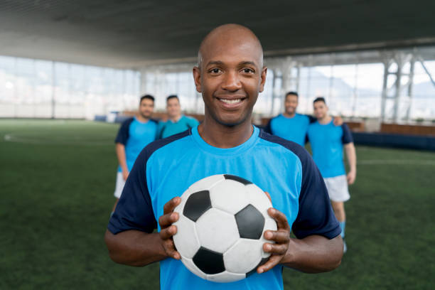 istock Cheerful black soccer player looking at camera smiling while holding a soccer ball 954392358