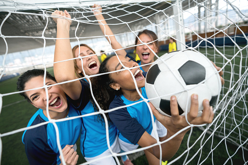 Excited female soccer players celebrating they scored a goal against the soccer net