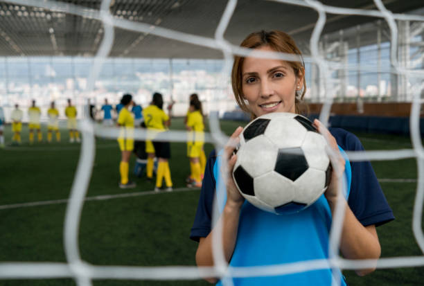 istock Professional female soccer player standing behind the net looking at camera smiling 954392580
