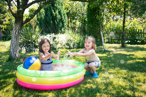 Two cute children having fun in inflatable swimming pool.