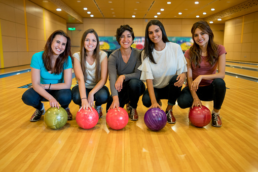 Group of female friends at the bowling alley looking at camera smiling very happy while kneeling down on the floor