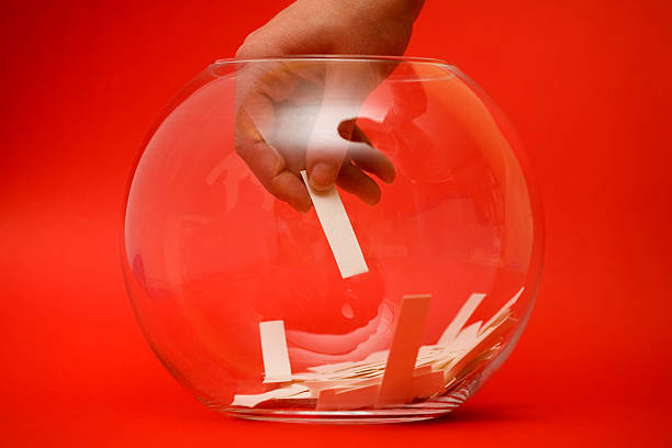 A hand selecting a paper ballot from a glass bowl on red stock photo