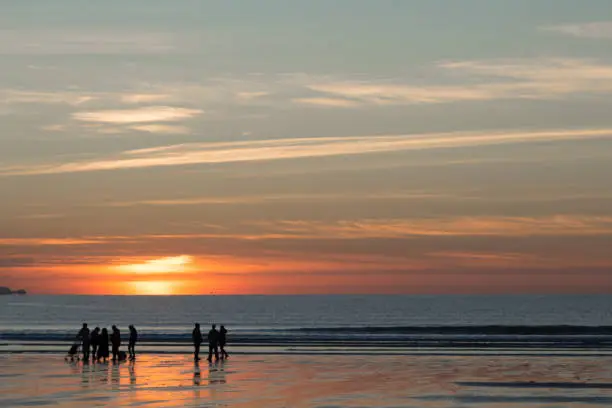 Silhouette of a family taking a walk on a beach on a calm day at sunset.