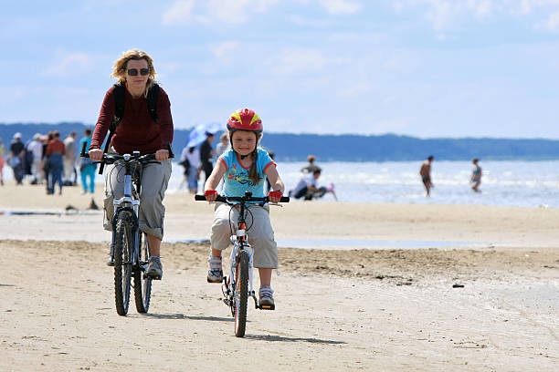 Mother and daughter riding along the beach stock photo