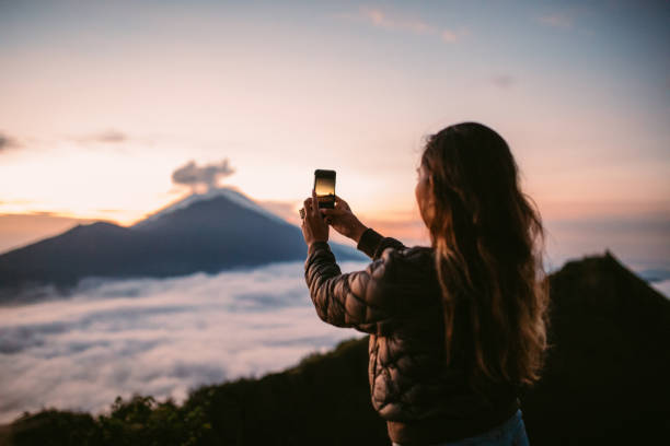 Photographing sunset One woman, standing high on beautiful mountain Batur in sunset alone, photographing sunset with smart phone. active volcano photos stock pictures, royalty-free photos & images