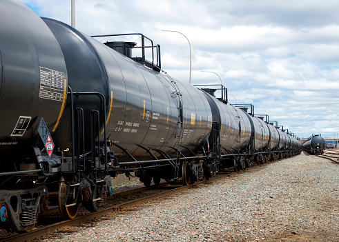 Black railway tanker cars of the type used to transport petroleum products. Several cars visible on two separate sets of tracks. Identification markings have been removed, only technical infomation remains.