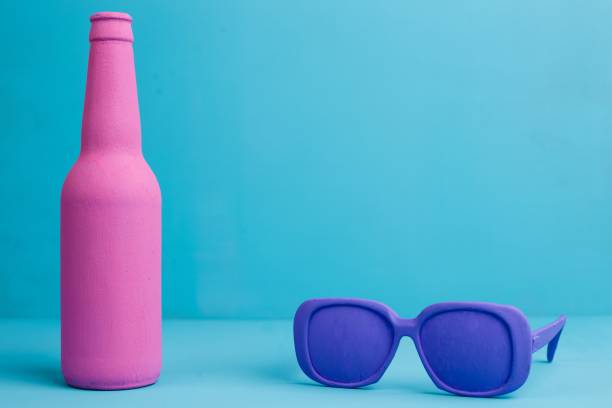 istock Pink bottle and violet retro style sunglasses on blue background 954475196