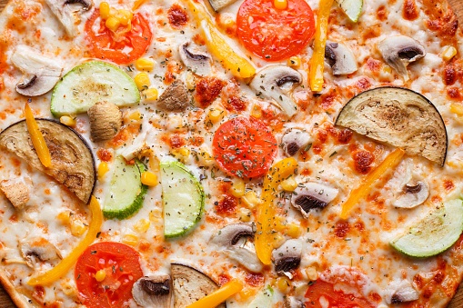 Pizza texture. Delicious Italian food. Fresh hot vegetarian pizza with tomato, zucchini, eggplant and mushrooms close up