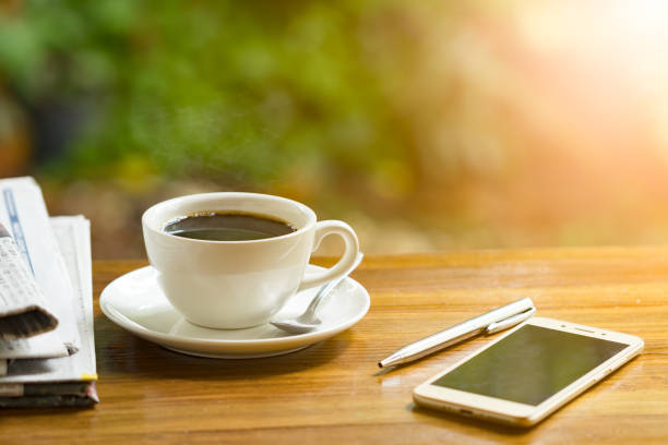 istock coffee cup with newspaper on a wooden table. Image is overexposed from the right bottom corner. 954478806