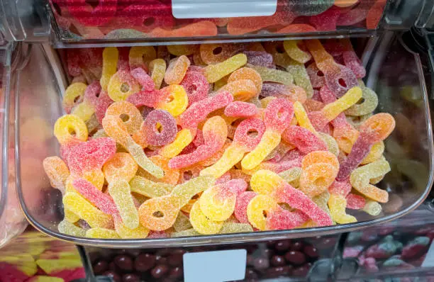 Photo of Closed up fizzy and sour gummy jelly in plastic container at confectionery shop.