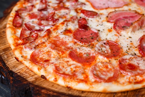 Delicious yummy fresh pizza with bacon, salami, ham and pepperoni and appetizing crust, close up. Italian food, pizzeria concept