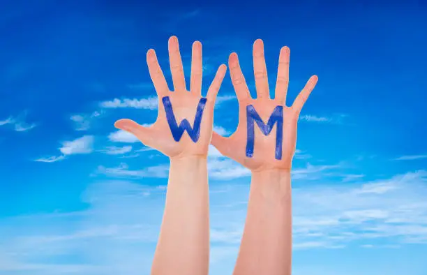 Many People Hands With Letters Building The German Word WM Means World Cup. Blue Cloudy Sky As Background