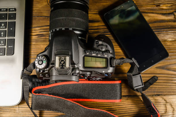 istock Modern DSLR camera, smartphone and laptop on wooden table. Top view 954495782