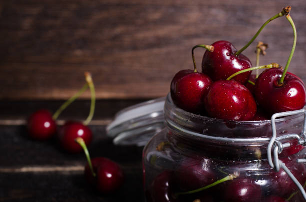istock Cherries in glass jar on wooden table. Free space for your text 954504582