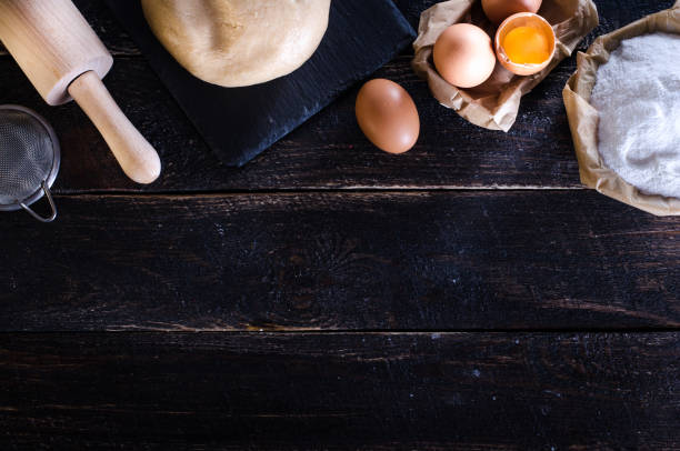 istock Ingredients for baking - dough, flour, wooden spoon, rolling pin, eggs, egg yolks on white background. Free space for your text 954505568