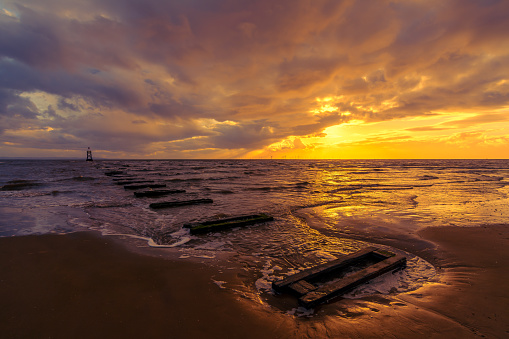 Golden sunset on incoming tide and old wooden jetty on Crosby Beach, Liverpool, England, UK.
