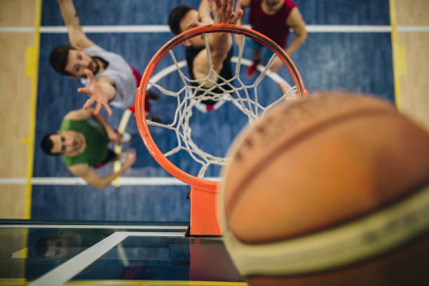 Above view of basketball match on the court. High angle view of basketball hoop in the focus during a match on the court. slam dunk basketball basketball hoop close up stock pictures, royalty-free photos & images
