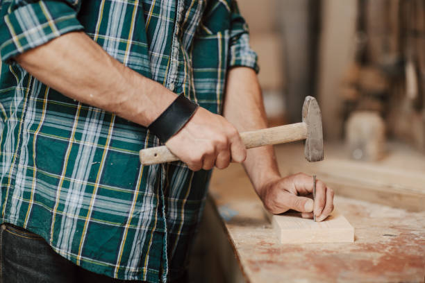istock Carpenter builder nailing wood board with hammer on a wooden table in the workshop. 954527898