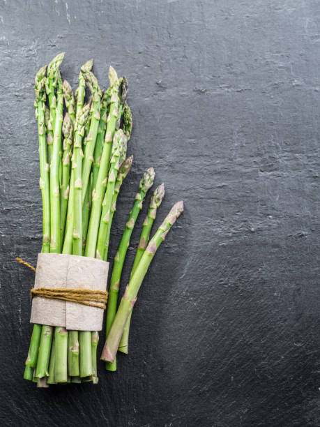 istock Green young asparagus sprouts on the black background. 954534406