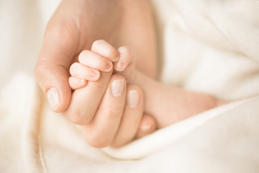 Female hand holding her newborn baby's hand. Mom with her child. Maternity, family, birth concept. Copy space for your text.