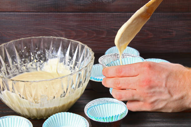 istock Hands pouring dough into molds for muffins on a wooden table. 954538962