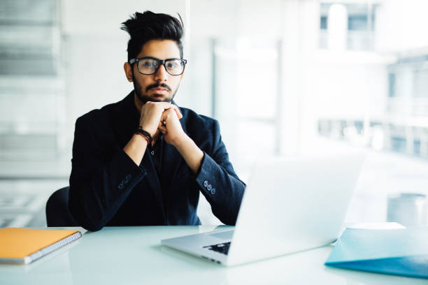 istock Indian business Man using laptop with hands hand on chin in his modern office 954552150