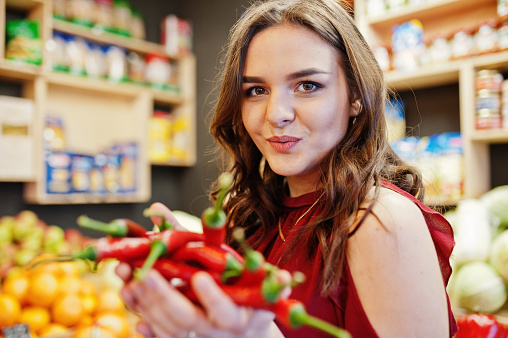 Girl in red holding hot chili peppers on fruits store.