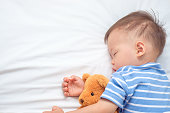 かわいいアジア幼児男の子の子供睡眠/テディー ・ ベアをテディベアで選択と集中を抱きしめながら毛布の下で昼寝をして