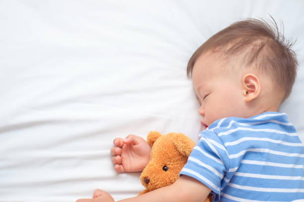 istock Cute Asian toddler boy child sleeping / taking a nap under blanket while hugging teddy bear, Selective focus at teddy 954552466