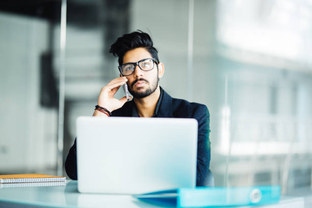 istock business, people and technology concept. Young businessman with laptop computer calling on smartphone at office 954553574