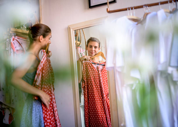 mulher olhando no espelho enquanto o vestido no quarto em uma loja. - cabine de loja - fotografias e filmes do acervo