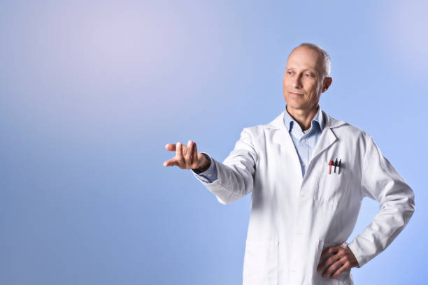 A good-looking mature male scientist looks thoughtful as he stands, one hand outstretched pointing towards blank space the other on his hip.