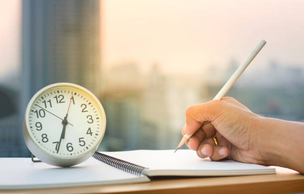 istock Hand hold pencil writing on note book with simple clock and blur sunset background. Concept Image for Working or Planning idea. 954570044