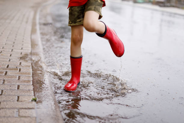 istock Child wearing red rain boots jumping into a puddle. 954587046