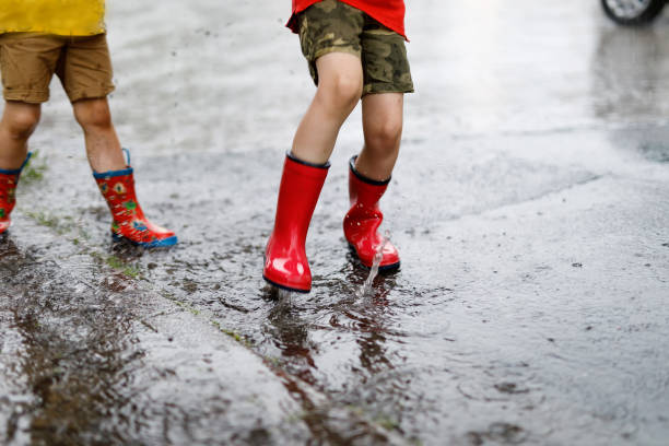 istock Two children wearing red rain boots jumping into a puddle. 954587716