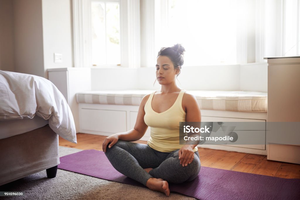 Beginning my day with meditation Shot of a beautiful young woman practicing yoga at home Meditating Stock Photo